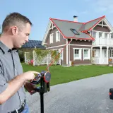 Mężczyzna używa dalmierza laserowego do precyzyjnego pomiaru, jak zmierzyć przekątną dachu domu.