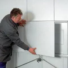 Mężczyzna montuje panel do ocieplenia bramy garażowej segmentowej.