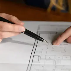 Rysunek techniczny z planem pomieszczenia, gdzie palcem i długopisem zaznaczono, jak obliczyć metry do malowania.