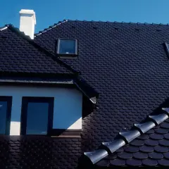 Ciemny dach z dachówki ceramicznej, z kominem i oknami dachowymi. Zastanawiasz się, ile waży paleta dachówki ceramicznej?