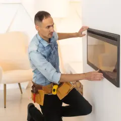 Instrukcja zabudowy kominka: mężczyzna w pasie z narzędziami montuje nowoczesny kominek elektryczny.