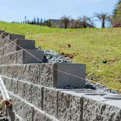Budowa fundamentu pod murek oporowy. Betonowe bloki układane są na zboczu, tworząc stabilną konstrukcję.
