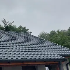 Szary dach z blachy, idealny przykład, jak uszczelnić dach przed deszczem. Wokół zielone drzewa.