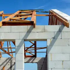 Budowa domu z silikatu, widoczny szkielet dachu z drewna na tle błękitnego nieba.
