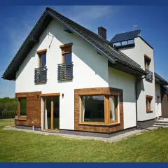 Nowoczesny dom z białym tynkiem, drewnianymi elementami i antracytowym dachem. Okna w kolorze winchester dodają elegancji.