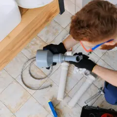 Hydraulik montuje syfon pod umywalką. Dowiedz się, ile kosztuje hydraulika w domu, gdy potrzebna jest fachowa pomoc.
