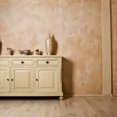 Elegancka komoda z crackle na drzwiach, inspirowana glinką wenecką, na tle ściany o ciepłej, rustykalnej fakturze.