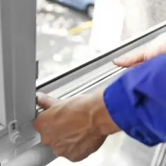 Ręce w niebieskiej koszuli montują uszczelkę, pokazując jak uszczelnić okna plastikowe.