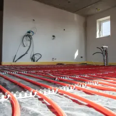 Instalacja podłogówki w garażu w trakcie budowy. Czerwone rurki systemu grzewczego ułożone na folii izolacyjnej.