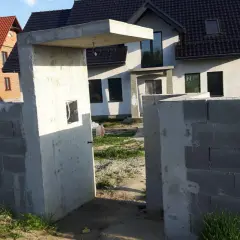 Betonowy daszek nad furtką, budowa ogrodzenia z pustaków, domy w tle.