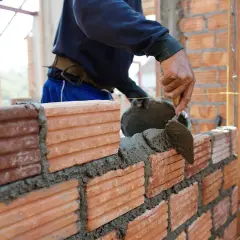 Murarz z kielnią układa cegły, tworząc ścianę. Zastanawiasz się, ile bierze murarz za swoją pracę?