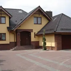 Dom z żółtą elewacją i brązowym dachem. Zastanawiasz się, ile waży dachówka? Ten dach wygląda solidnie.