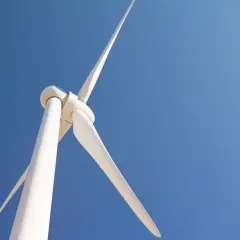 Biała turbina wiatrowa na tle błękitnego nieba. Zastanawiasz się, ile kosztuje elektrownia wiatrowa?