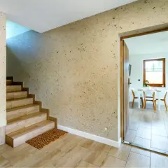 Nowoczesny tynk dekoracyjny na klatce schodowej dodaje wnętrzu charakteru. Drewniane schody i drzwi tworzą ciepłą atmosferę.