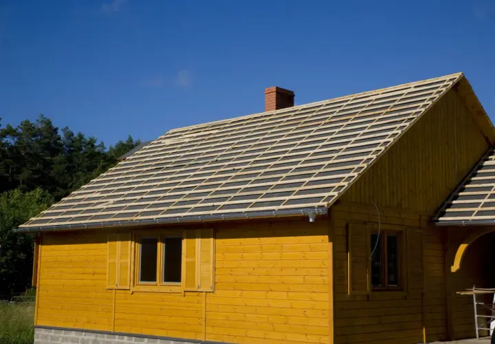 Dach drewnianego domu w budowie, przygotowany pod deskowanie pod blachodachówkę. Widać rusztowanie i komin.