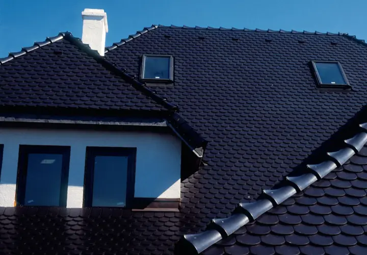 Ciemny dach z dachówki ceramicznej, z kominem i oknami dachowymi. Zastanawiasz się, ile waży paleta dachówki ceramicznej?