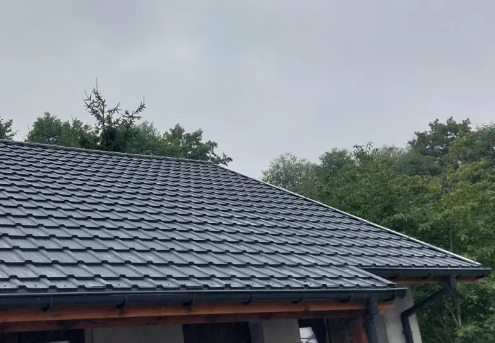 Szary dach z blachy, idealny przykład, jak uszczelnić dach przed deszczem. Wokół zielone drzewa.