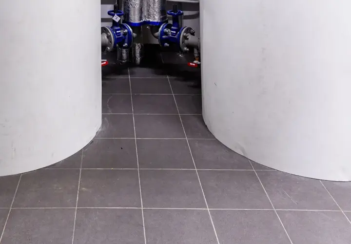 Kotłownia w płytkach. Dwa białe cylindry otaczają instalację hydrauliczną z niebieskimi zaworami.