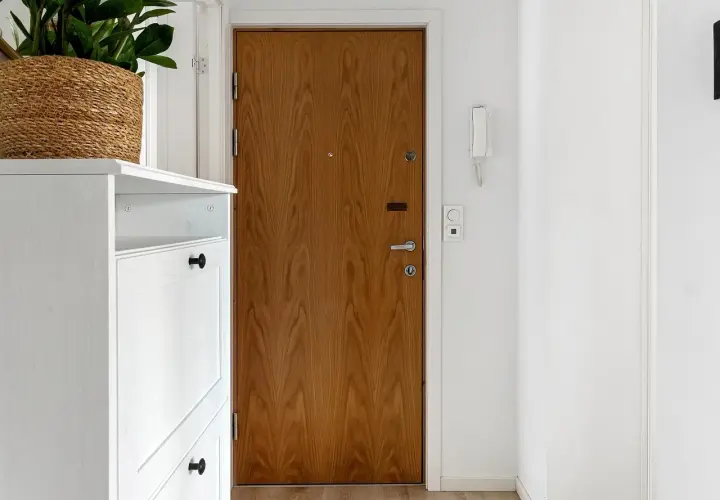 Biały mebel na buty, drewniane drzwi i na jakiej wysokości wideodomofon.