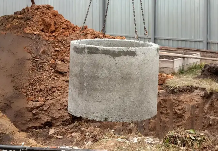 Betonowy krąg opuszczany do wykopu. Zastanawiasz się, ile kosztuje założenie szamba? To pierwszy krok do jego budowy.