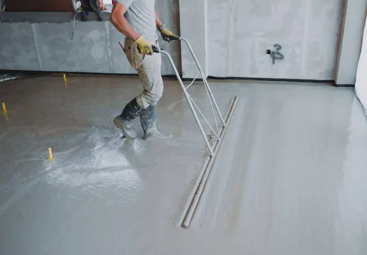 Pracownik wykonuje posadzki z miksokreta, wyrównując świeży beton specjalnym narzędziem.
