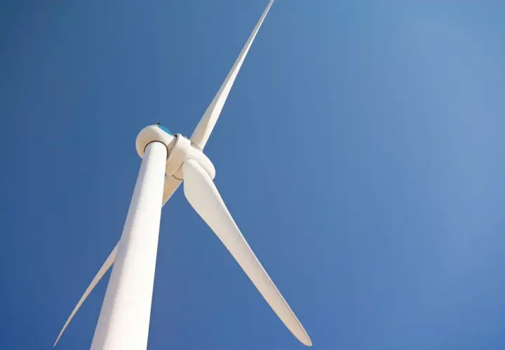 Biała turbina wiatrowa na tle błękitnego nieba. Zastanawiasz się, ile kosztuje elektrownia wiatrowa?