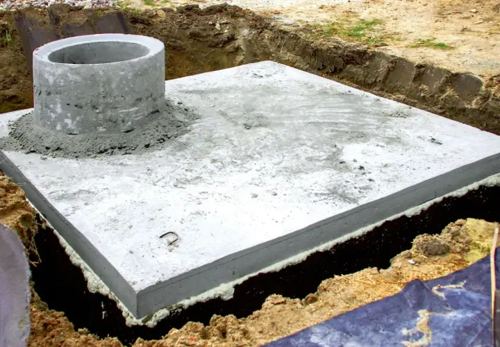 Betonowa płyta fundamentowa z kominem szamba, przygotowana do dalszych prac. Zastanawiasz się, ile kosztuje montaż szamba?