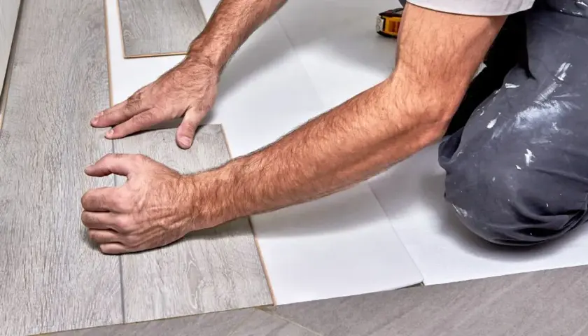 Ręce układają panele laminowane na podkładzie, pokazując, jak położyć płytki na dylatacji.