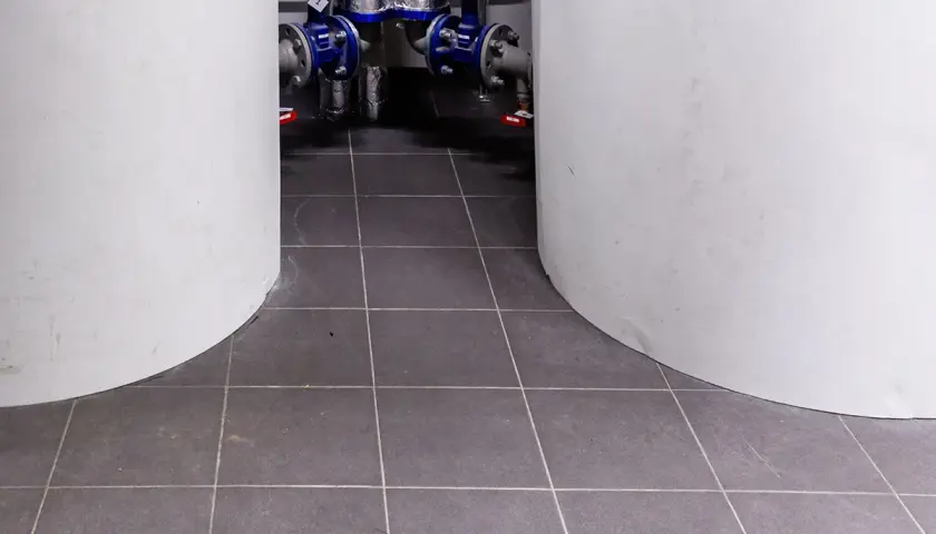 Kotłownia w płytkach. Dwa białe cylindry otaczają instalację hydrauliczną z niebieskimi zaworami.