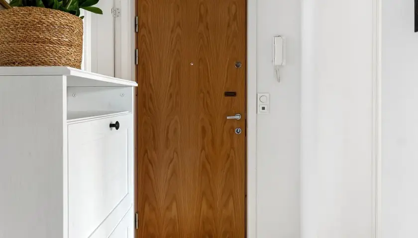 Biały mebel na buty, drewniane drzwi i na jakiej wysokości wideodomofon.