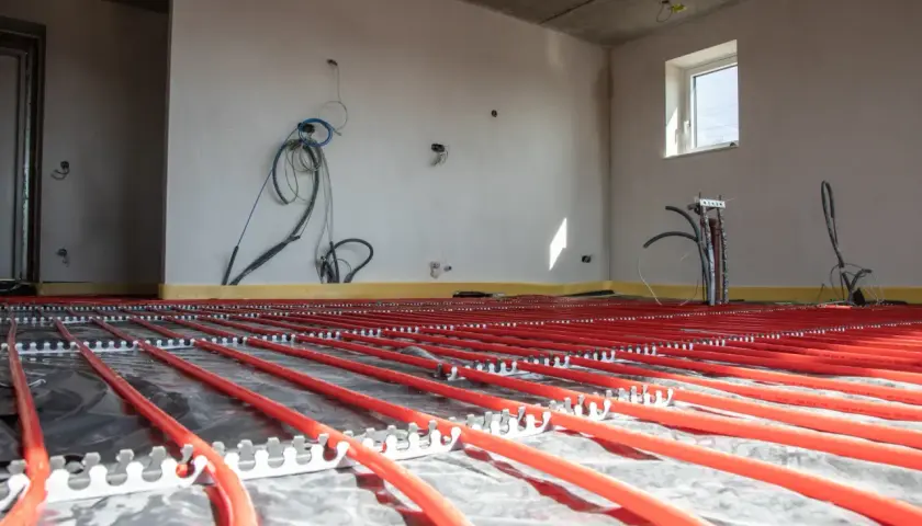 Instalacja podłogówki w garażu w trakcie budowy. Czerwone rurki systemu grzewczego ułożone na folii izolacyjnej.