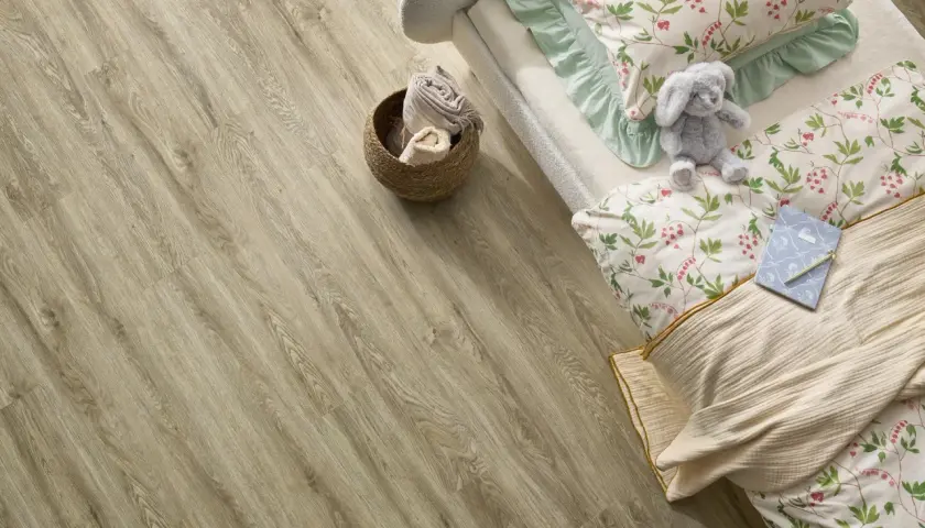 Łóżko z pluszowym królikiem i pościelą w kwiaty na podłodze z paneli winylowych. Czy panele winylowe są zdrowe? Tak, są bezpieczne dla dzieci.