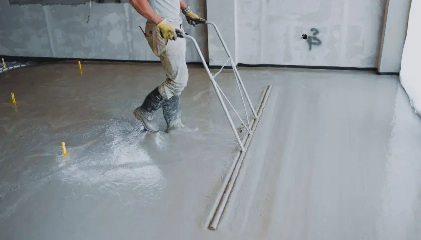 Pracownik wykonuje posadzki z miksokreta, wyrównując świeży beton specjalnym narzędziem.