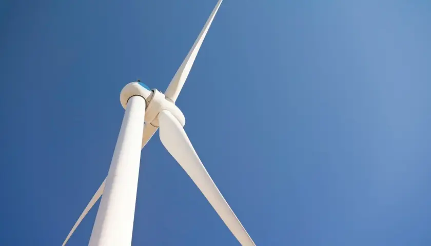Biała turbina wiatrowa na tle błękitnego nieba. Zastanawiasz się, ile kosztuje elektrownia wiatrowa?