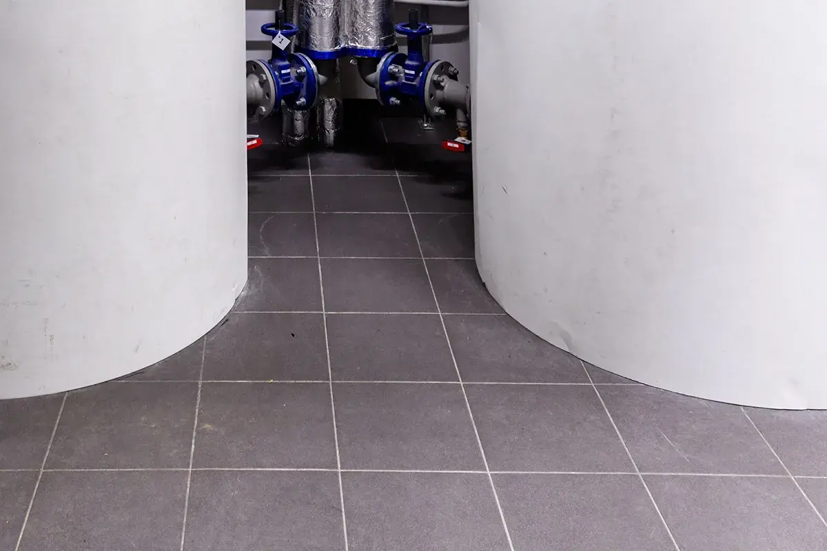 Kotłownia w płytkach. Dwa białe cylindry otaczają instalację hydrauliczną z niebieskimi zaworami.