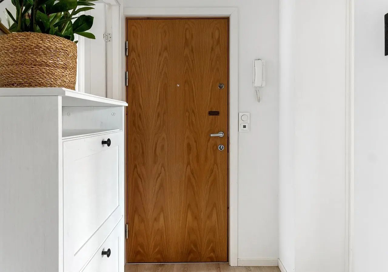 Biały mebel na buty, drewniane drzwi i na jakiej wysokości wideodomofon.