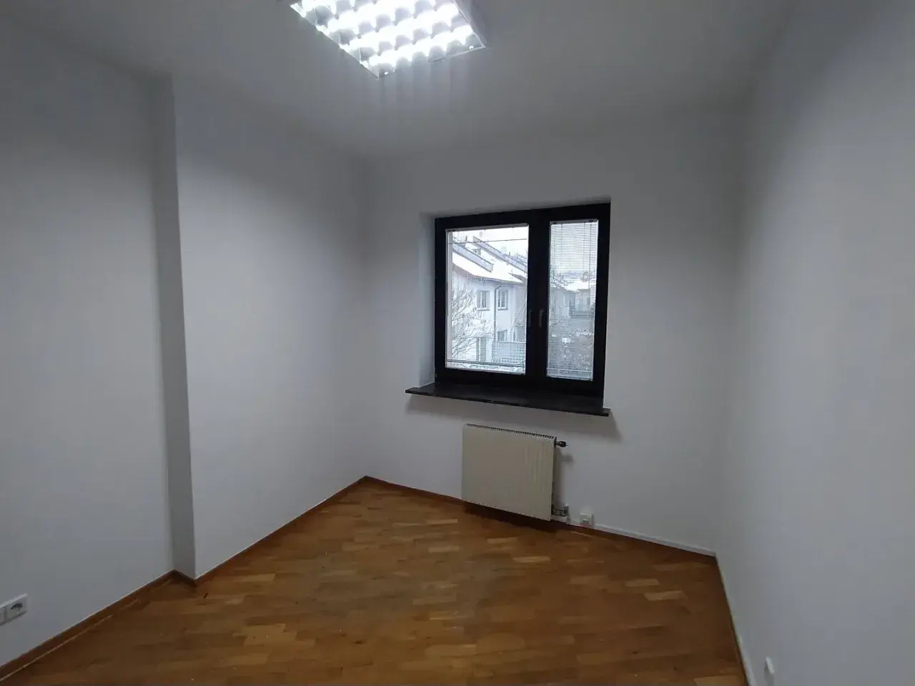 Puste pomieszczenie z drewnianą podłogą i oknem. Zastanawiasz się, ile trwa malowanie mieszkania?