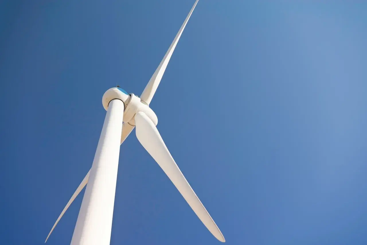 Biała turbina wiatrowa na tle błękitnego nieba. Zastanawiasz się, ile kosztuje elektrownia wiatrowa?