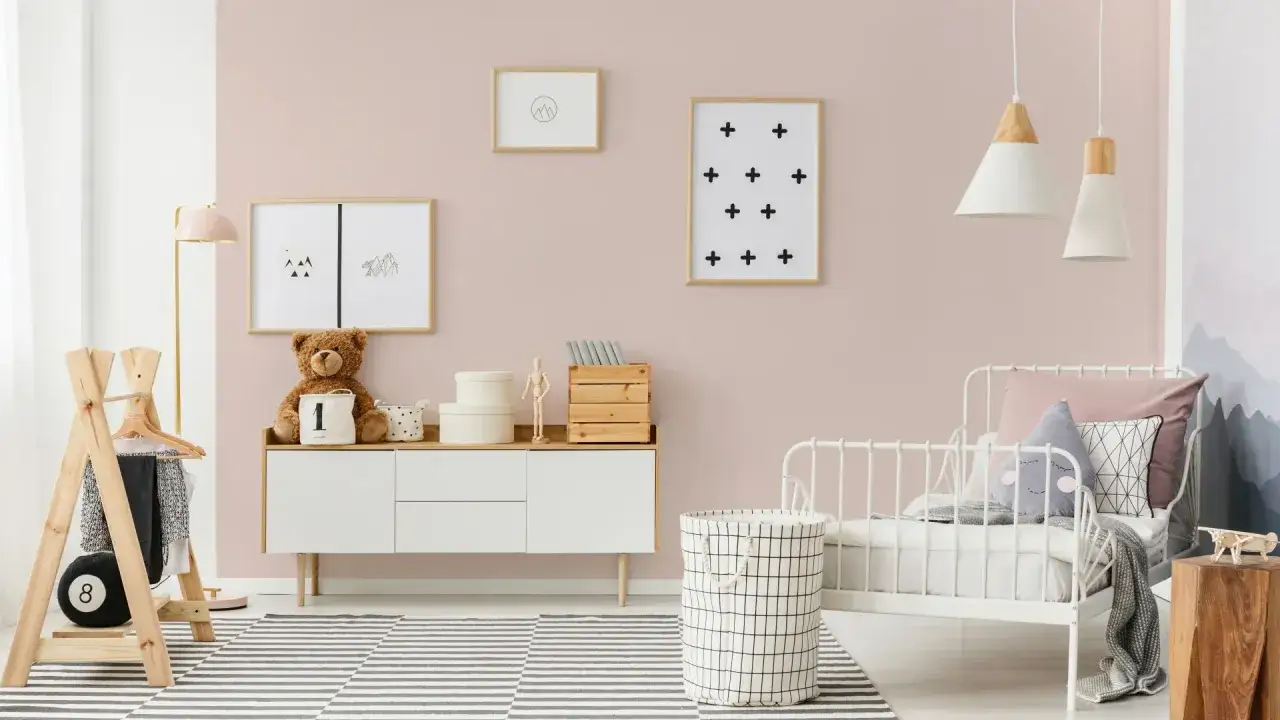 Pokój dziecięcy z łóżeczkiem, komodą i pluszowym misiem. Różowa ściana, dywan w paski, lampy. Beckers vaggfarg a designer różnica w kolorze ścian.