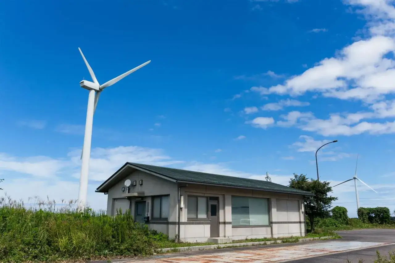 Wiatrak i budynek na tle błękitnego nieba. Zastanawiasz się, ile kosztuje elektrownia wiatrowa?