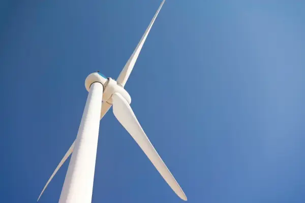 Biała turbina wiatrowa na tle błękitnego nieba. Zastanawiasz się, ile kosztuje elektrownia wiatrowa?